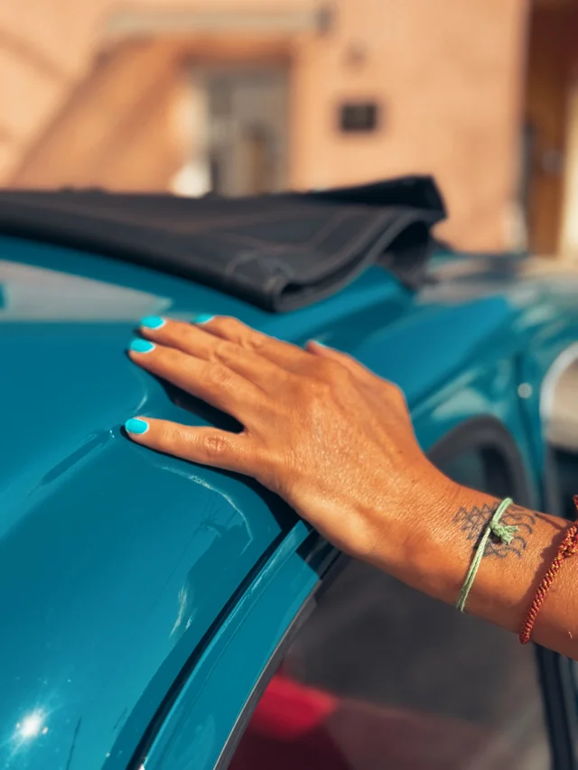 A hand resting on the turquoise door of a vintage Fiat 500