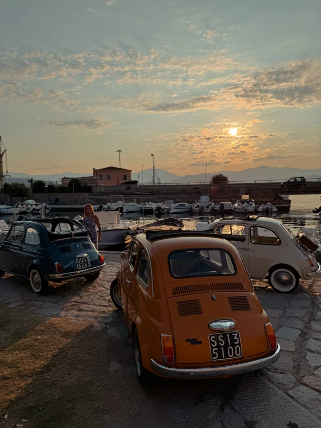 Vintage Fiat 500 cars parked beside the harbour at sunset